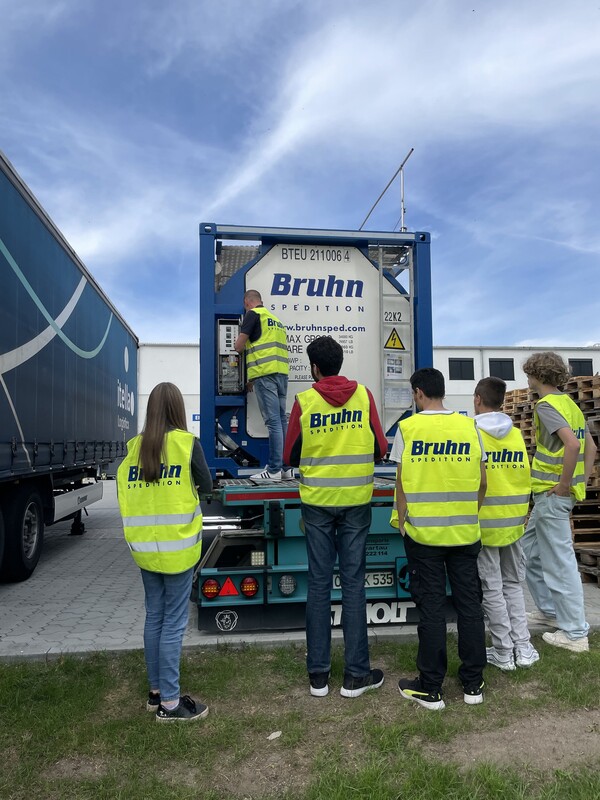 Azubirallye Gruppe von Mitarbeitenden in Warnwesten bei einer Containerdemonstration auf dem Firmengelände